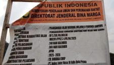 Papan informasi proyek rehabilitasi jalan dan pembangunan Jembatan Gantung Way Besai, Way Kanan, yang dikerjakan oleh Satker Pelaksanaan Jalan Nasional Wilayah II Provinsi Lampung. Proyek ini menjadi sorotan warga terkait dugaan penggunaan material batu bulat berukuran kecil pada pekerjaan pemasangan bronjong di lokasi. Foto: Tikampost.id/Marto