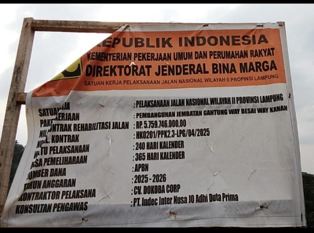 Papan informasi proyek rehabilitasi jalan dan pembangunan Jembatan Gantung Way Besai, Way Kanan, yang dikerjakan oleh Satker Pelaksanaan Jalan Nasional Wilayah II Provinsi Lampung. Proyek ini menjadi sorotan warga terkait dugaan penggunaan material batu bulat berukuran kecil pada pekerjaan pemasangan bronjong di lokasi. Foto: Tikampost.id/Marto