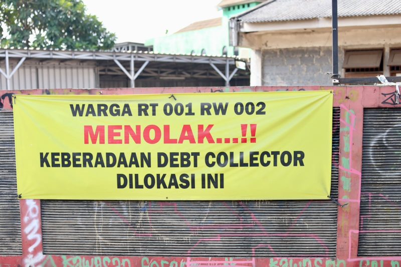 Spanduk penolakan terhadap aktivitas debt collector terpasang di kawasan RT 001/RW 002 sebagai bentuk aspirasi warga yang menginginkan lingkungan tetap aman, tertib, dan bebas dari potensi keributan di ruang publik. Warga berharap setiap proses penagihan pembiayaan dilakukan sesuai ketentuan hukum tanpa mengganggu ketertiban masyarakat.
Foto: Dok. Tikampost.id.