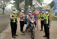 Personel Polres Dharmasraya membagikan masker kepada masyarakat yang melintas di Jalan Lintas Sumatera (Jalinsum), kawasan Gunung Medan, Kecamatan Sitiung, Kamis (8/10/2026), di tengah kondisi kabut asap