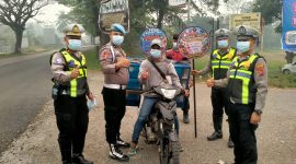 Personel Polres Dharmasraya membagikan masker kepada masyarakat yang melintas di Jalan Lintas Sumatera (Jalinsum), kawasan Gunung Medan, Kecamatan Sitiung, Kamis (8/10/2026), di tengah kondisi kabut asap