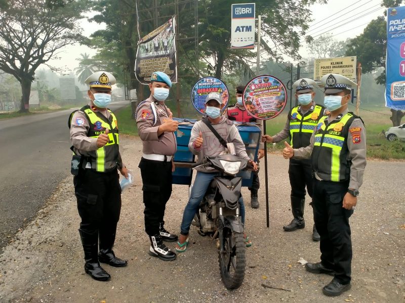 Personel Polres Dharmasraya membagikan masker kepada masyarakat yang melintas di Jalan Lintas Sumatera (Jalinsum), kawasan Gunung Medan, Kecamatan Sitiung, Kamis (8/10/2026), di tengah kondisi kabut asap